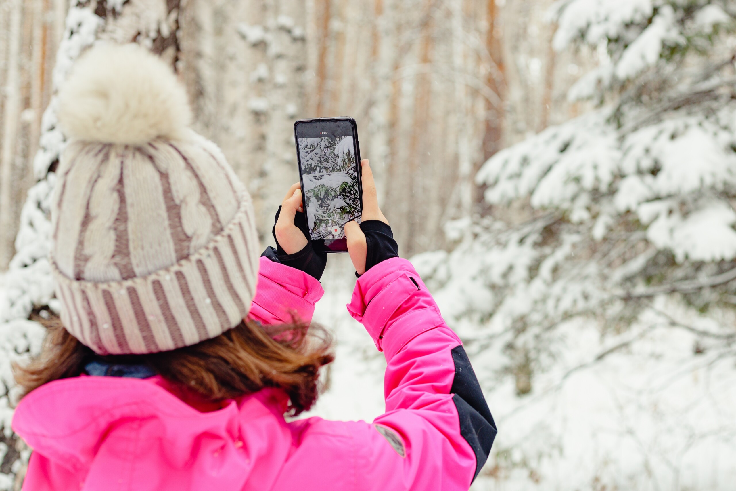 Nainen ottaa valokuvaa kännykällä talvisessa metsässä.